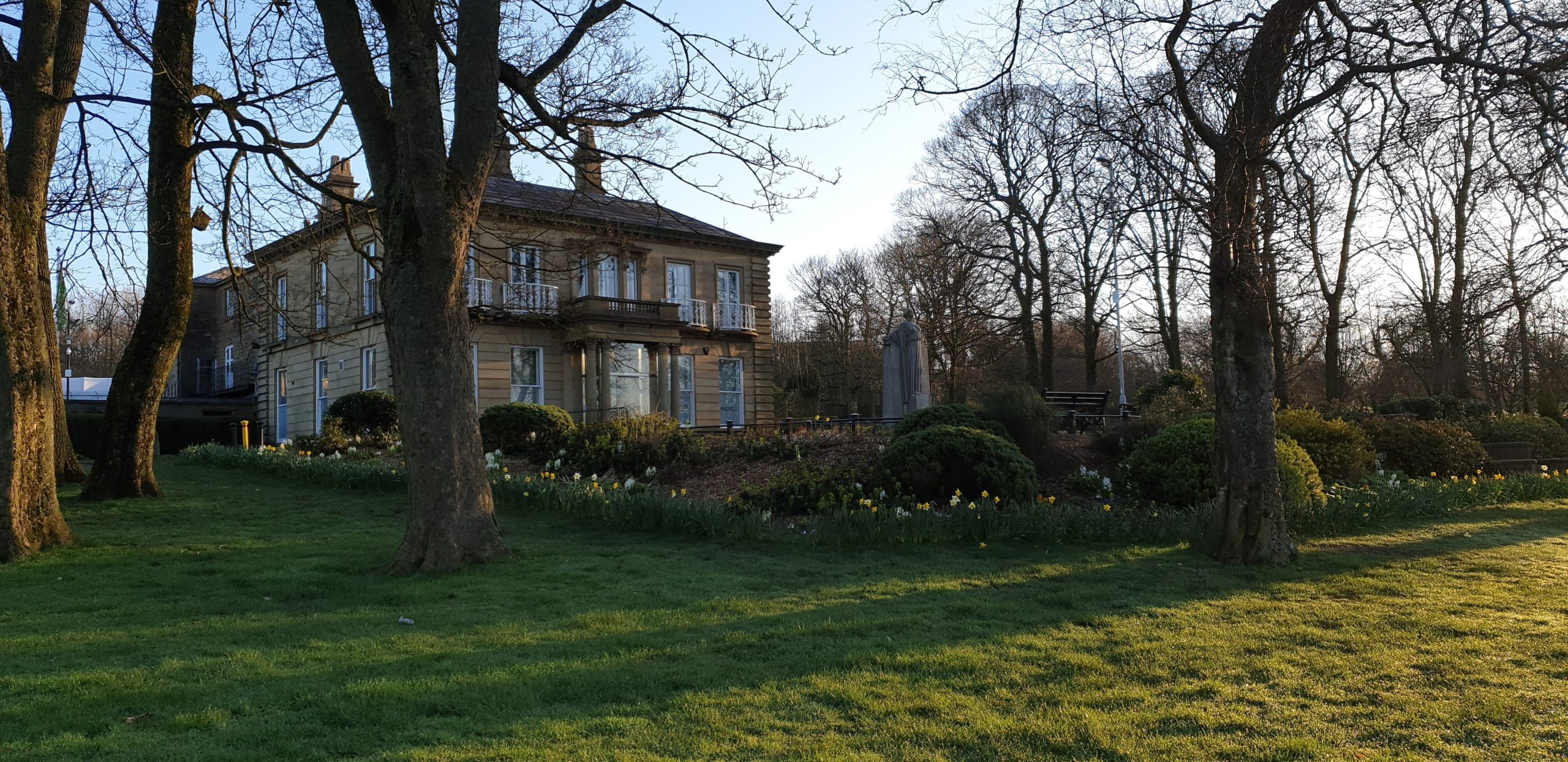 Large house with a balcony overlooking a garden with trees and grass.