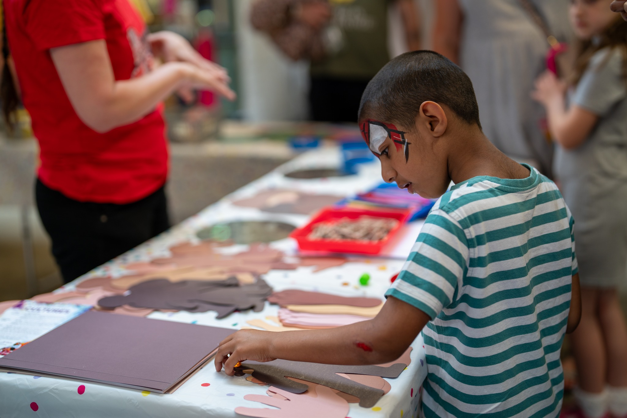 Child with face paint at crafting table, Connecting Cultures Event