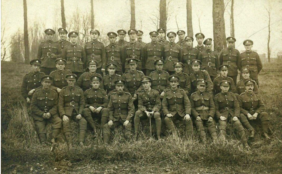 Group photograph of uniformed soldiers posed outdoors on a grassy slope with trees in the background.