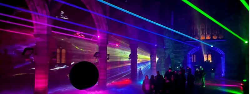 Colourful laser beams and fog filling a large arched hall as a group of people view the immersive light installation.