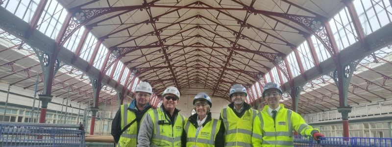 Five people in high visibility jackets and helmets, inside Market Hall