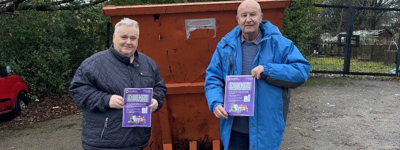 Two Councillors holding bulky waste collection leaflets infront of large, orange skip