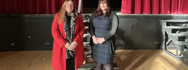 Two Councillors inside theatre with steps to stage and red theatre curtains in background