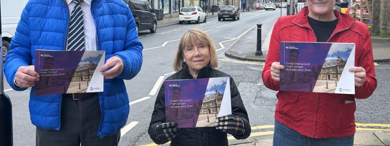 Three people holding a document with a high street in the background