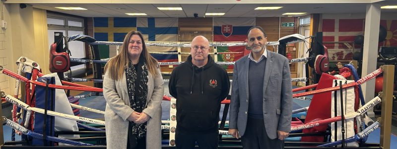 Three people standing in front of boxing ring with inspirational messages painted on the walls behind.