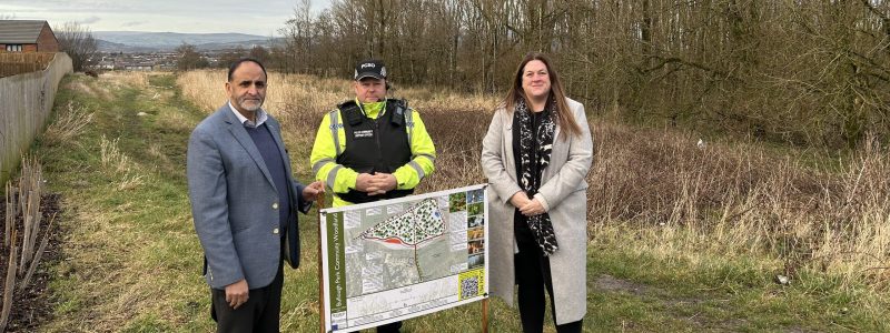 Three people including police officer with grass and woodland in background