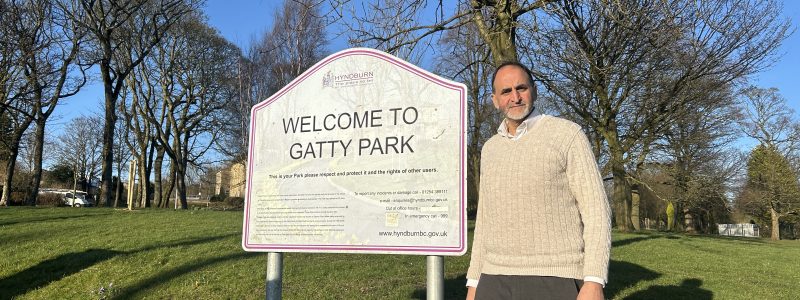 A person in a park next to a sign which reads Welcome to Gatty Park