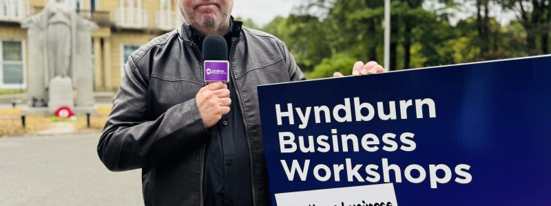A person holding a "Hyndburn Business Workshops" sign