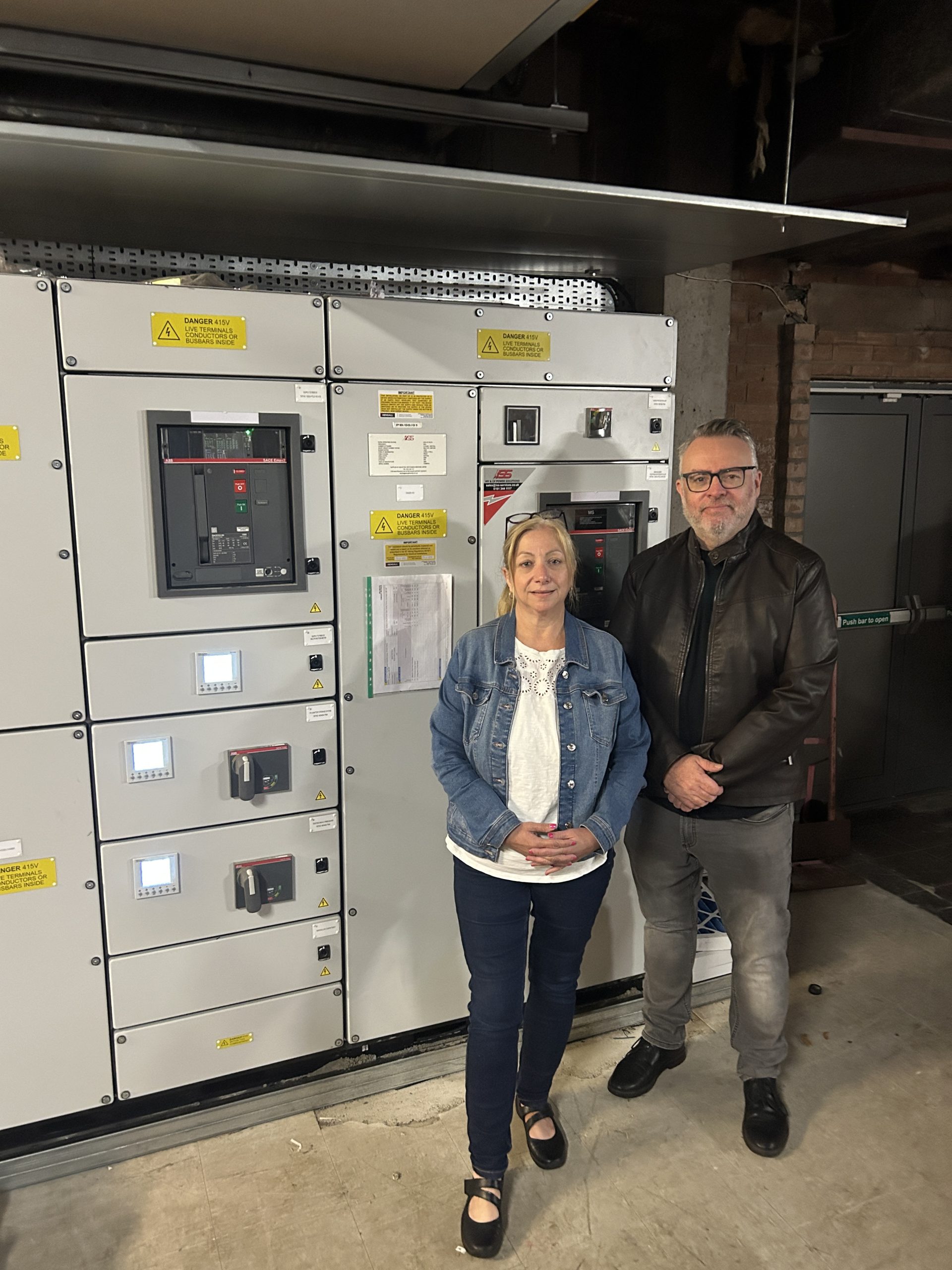 Two people in front of large electrical unit