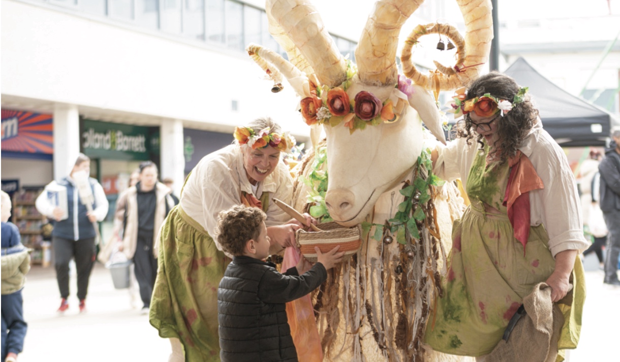 Child interacting with a costumed goat character at a public event.
