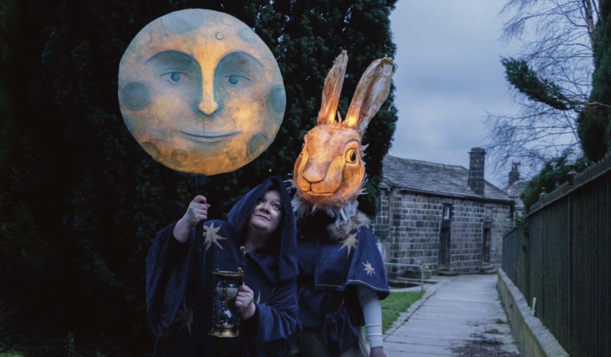 Two costumed figures holding illuminated moon and hare lanterns outdoors.