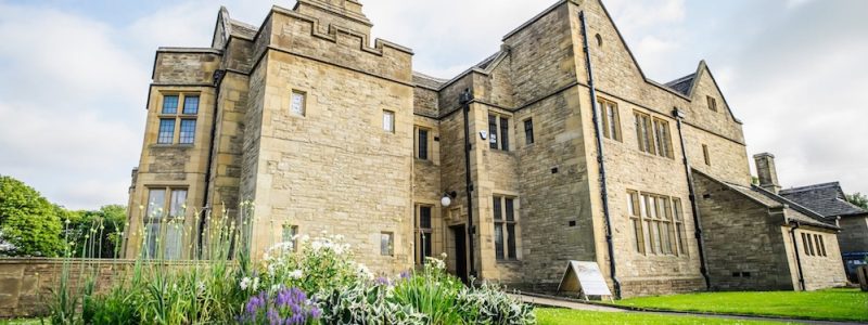 Historic stone building with a lawn and flower border.